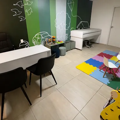 Consultório infantil com parede verde ilustrada, tapete colorido e mesinha para crianças