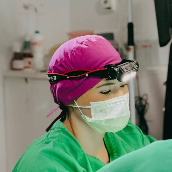 Profissional de saúde com touca e máscara durante procedimento na clínica